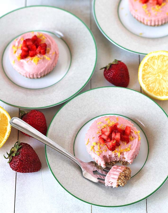 Overhead shot of Vegan Lemon Strawberry Cheesecake Bites on plates with fresh strawberries and a halved lemon sitting on either side of the plates