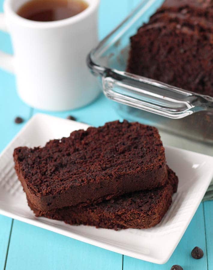 A plate of sliced Vegan Gluten Free Chocolate Zucchini Bread sitting on a plate on a blue table