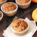 Vegan Gluten Free Pumpkin Spice Muffins sitting on a cooling rack with one muffin sitting on two pieces of parchment paper