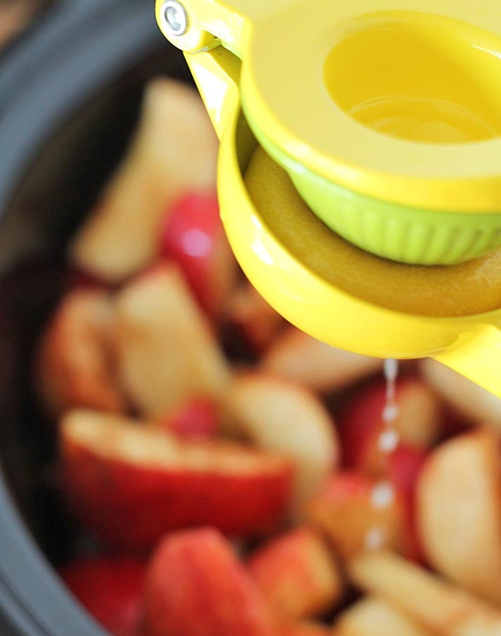 Cut apples in a slow cooker and a lemon squeezer above with lemon juice being squeezed onto the apples