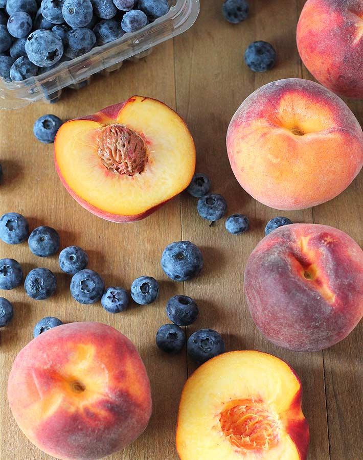 Peaches and blueberries on a wooden table, ingredients to make a Vegan Peach Blueberry Crisp