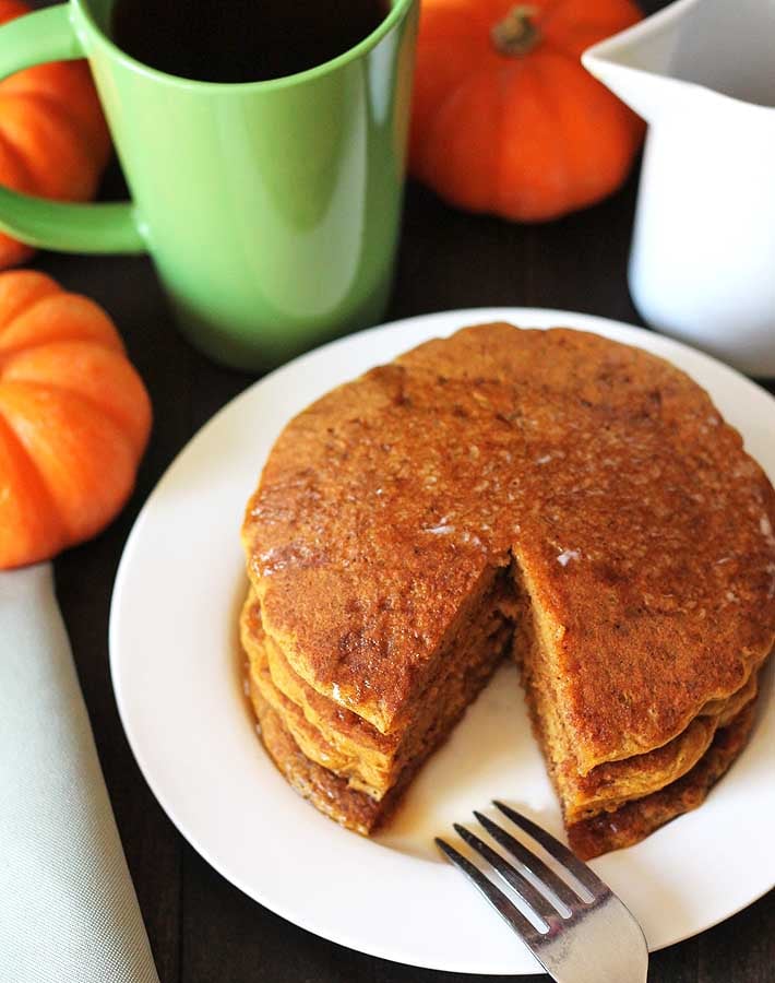 An overhead shot of a stack of vegan gluten free pumpkin pancakes on a plate with a fork sitting on the side