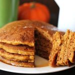 A stack of four vegan gluten free pumpkin pancakes with a wedge cut out of them