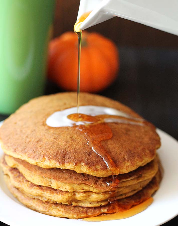Maple syrup being poured onto a stack of vegan gluten free pumpkin pancakes