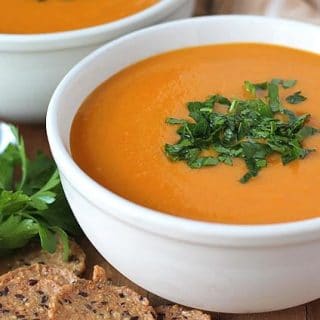 A white bowl filled with Butternut Squash Sweet Potato Carrot Soup with a garnish of chopped parlsey on top of the soup.