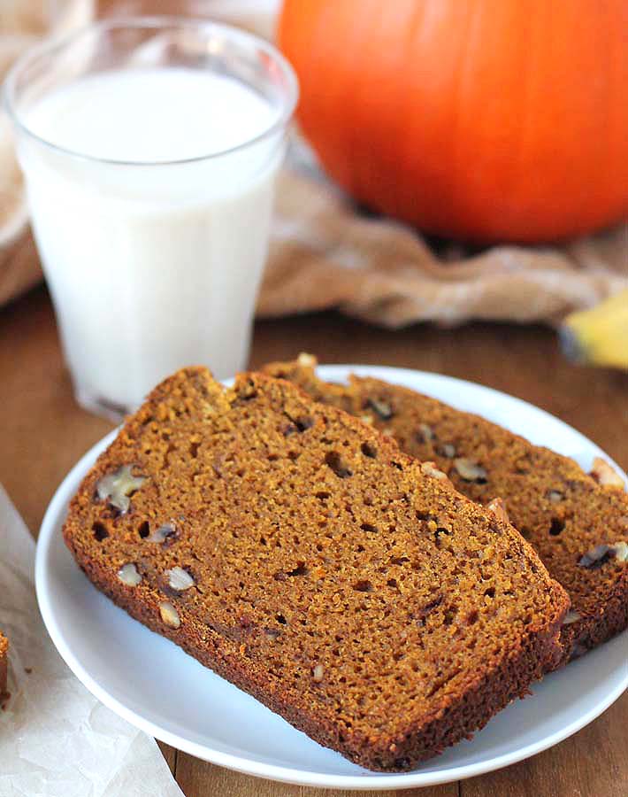 Two slices of Vegan Gluten Free Pumpkin Banana Bread on a plate with a glass of almond milk sitting behind it.