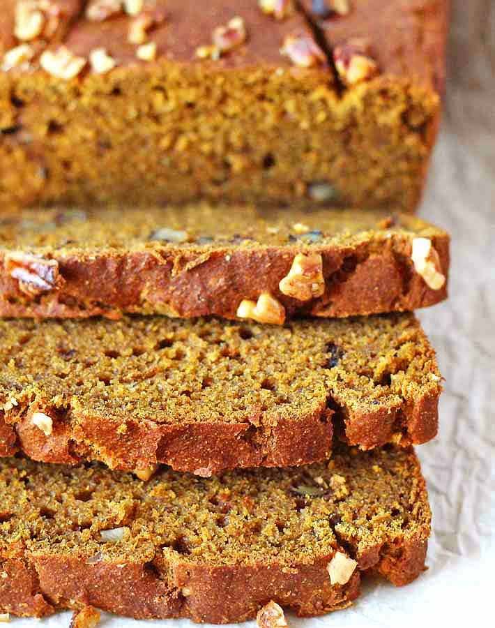 An up close shot of a loaf of Vegan Gluten Free Pumpkin Banana Bread with three slices in front of it.