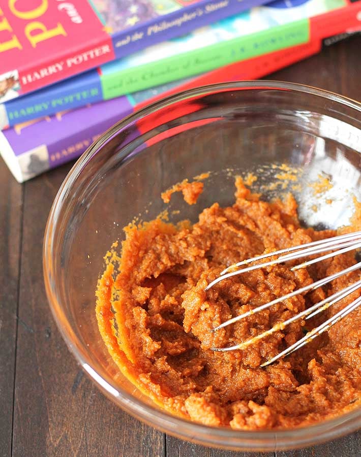 The filling for this Harry Potter pumpkin pasties recipe in a glass mixing bowl with a small whisk also in the bowl, three Harry Potter books are behind the bowl.