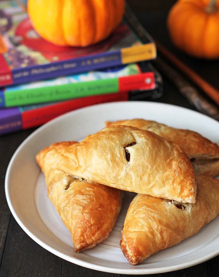  Una toma de cerca de empanadas fáciles de hacer sentadas en un plato con mini calabazas y tres libros de Harry Potter sentados detrás del plato.