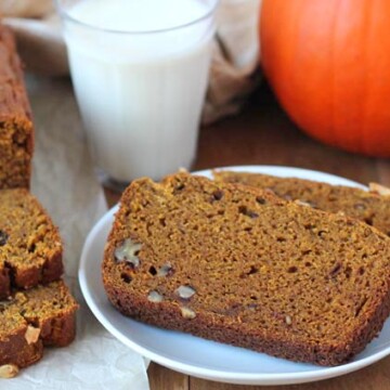 Two slices of Pumpkin Banana Bread on a small white plate, the full loaf sits on the left.