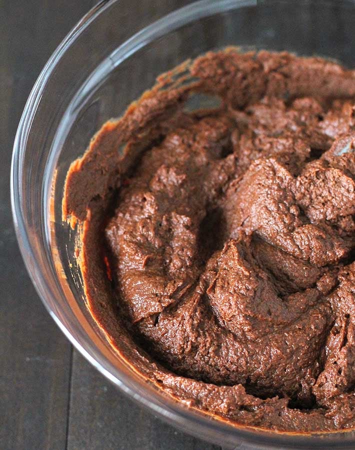 Vegan chocolate pumpkin pie filling in a glass mixing bowl sitting on a dark wood table.