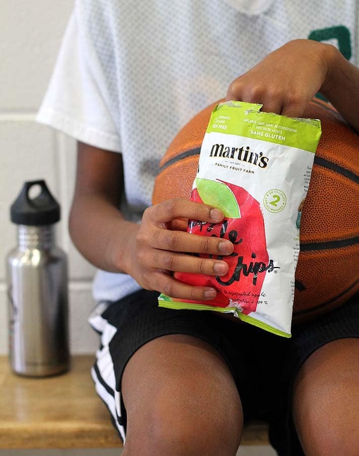 Vegan Snack Ideas for Active Kids plus an Easy Yogurt Dip Recipe: Child sitting on basketball game sidelines eating apple chips from a bag.