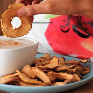 A hand dipping an apple chip into a bowl of yogurt dip.