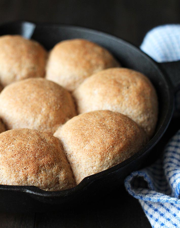 Vegan spelt rolls in a cast iron pan just out of the oven sitting on a dark wood table.