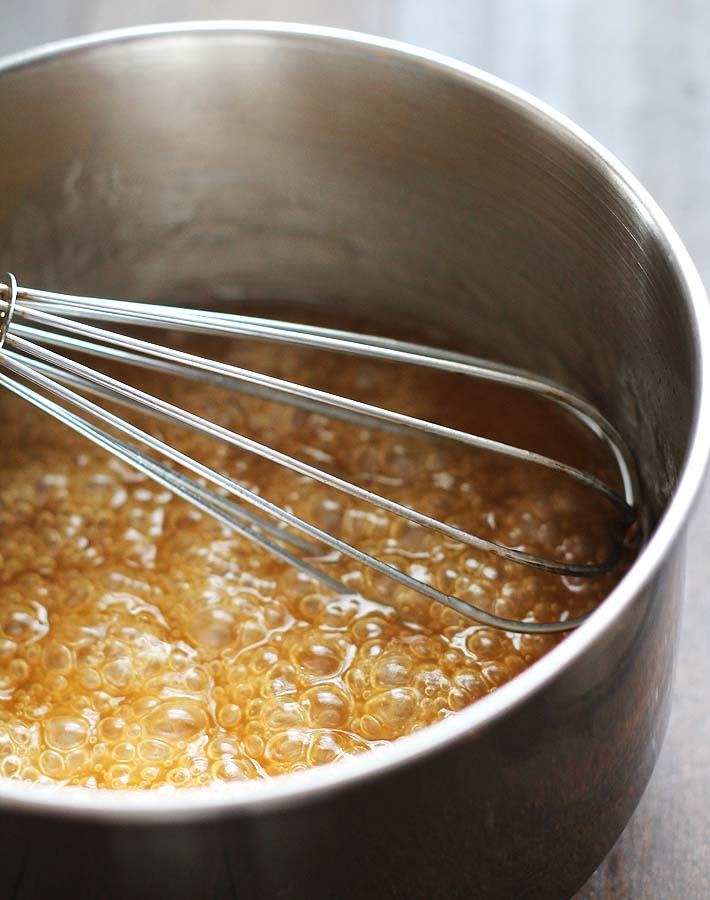 Maple caramel sauce simmering in a small stainless steel pot with a small wire whisk sitting in the pot.
