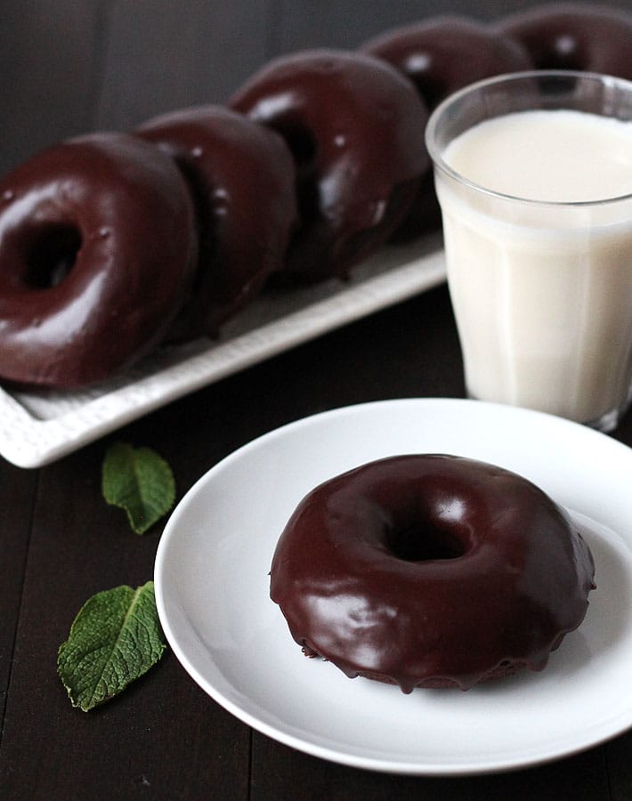 Vegan Gluten Free Chocolate Mint Doughnuts sitting on a white rectangle plate and one doughnut sitting on a small white plate with a glass of almond milk to the right of the small white plate.