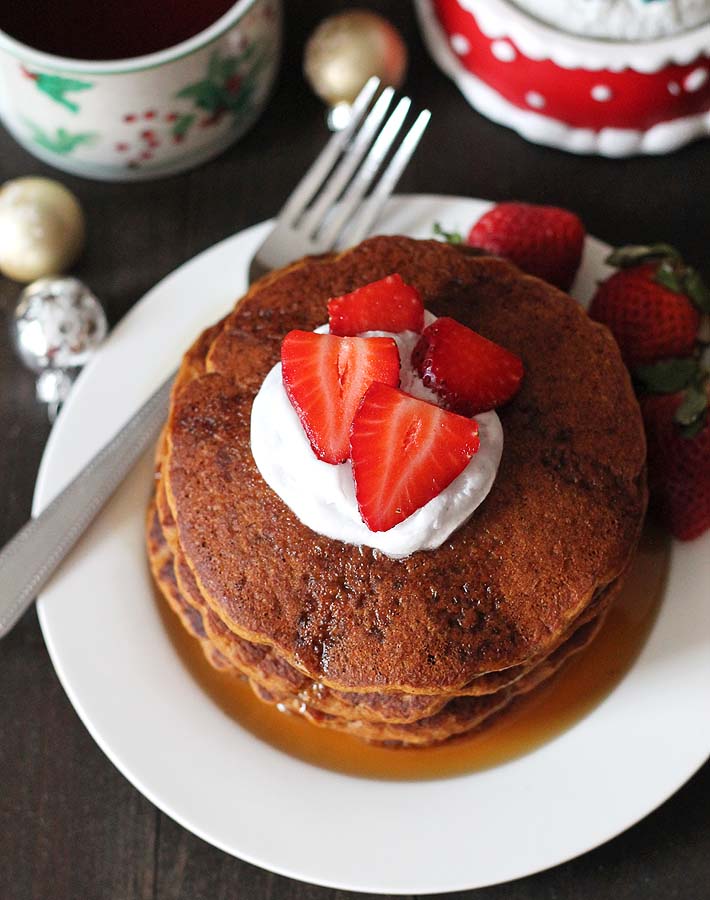 An overhead shot of Gluten Free Vegan Gingerbread Pancakes on a white plate with three fresh strawberries sitting on the right side of the plate and a fork sitting on the left.