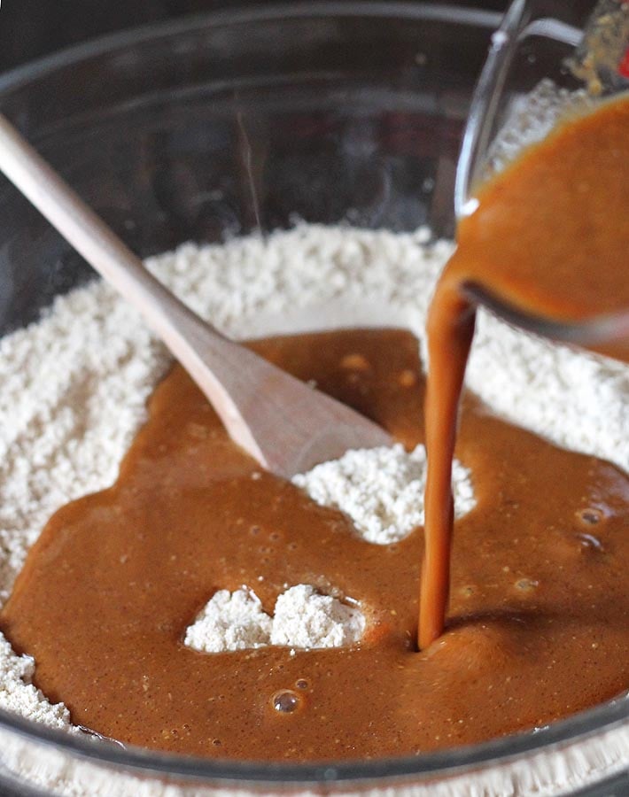 The wet mixture for Gluten Free Vegan Gingerbread Pancakes being poured into the dry mixture in a glass mixing bowl.