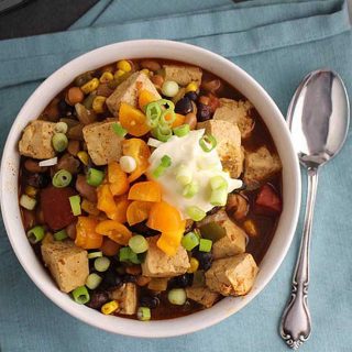 Easy Instant Pot Vegan Recipes - Overhead shot of Instant Pot vegan chili in a bowl on a blue tablecloth with a spoon to the right of the bowl.