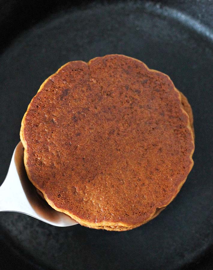 Gluten Free Vegan Gingerbread Pancakes being flipped over a cast iron skillet.