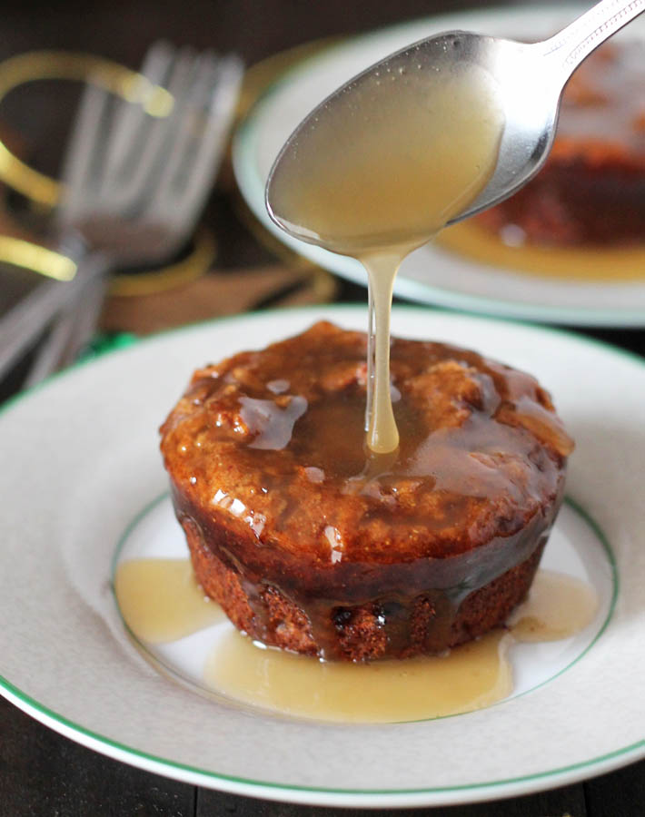 A spoonful of caramel sauce being drizzled onto a vegan sticky toffee pudding.