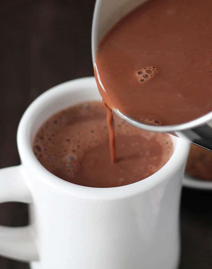 Creamy Vegan Hot Chocolate being poured from a small pot into a white mug.