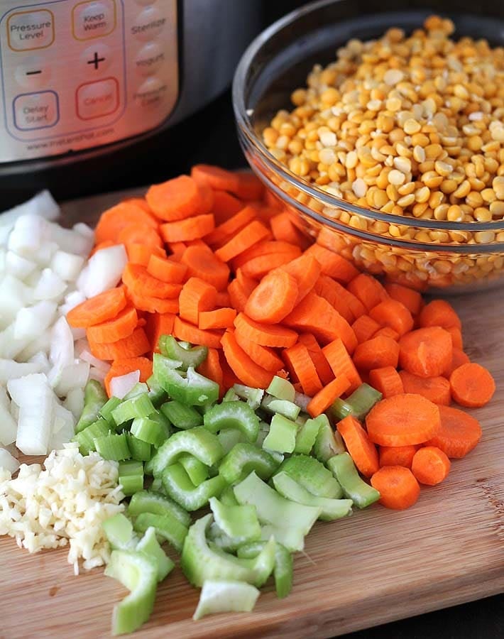 Chopped ingredients for Curried Instant Pot Split Pea Soup on a cutting board with a bowl of raw split peas sitting behind it and an Instant Pot sitting off to the left in the background.