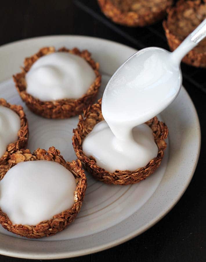 Vegan coconut yogurt being spooned into granola cups on a plate.