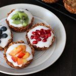 Four granola cups sitting on a white plate, each one is filled with yogurt and fresh fruit.