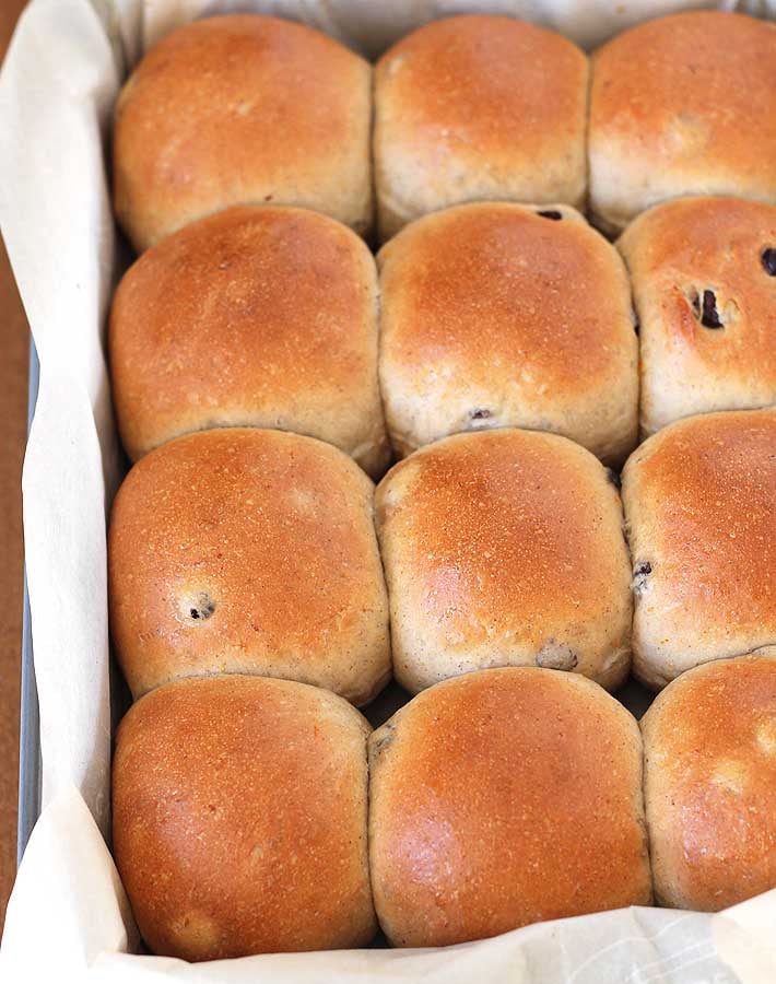 Overhead shot of fresh rolls just out of the oven sitting in a parchment lined baking pan, rolls were brushed with a vegan egg wash before baking to give them their golden tops.