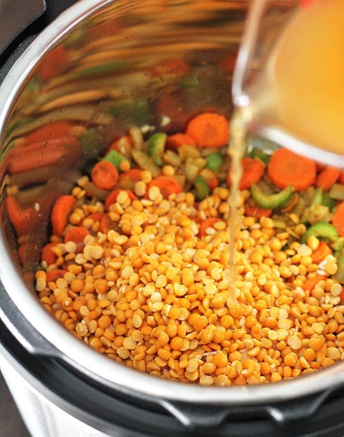 Broth being poured into a pot filled with ingredients for split pea soup.