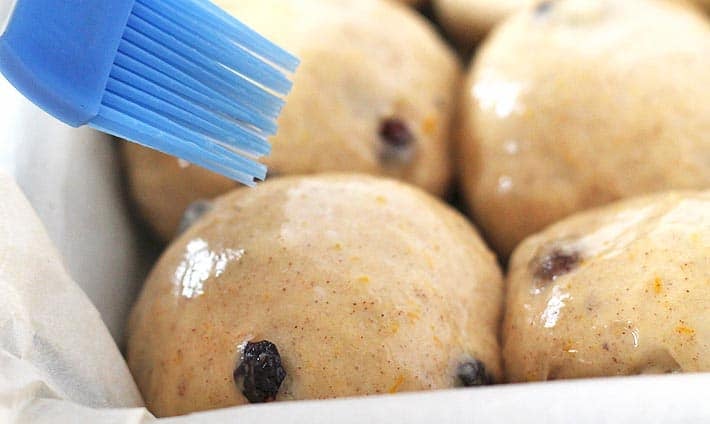 Vegan egg wash being brushed onto rolls with a blue silicone brush.