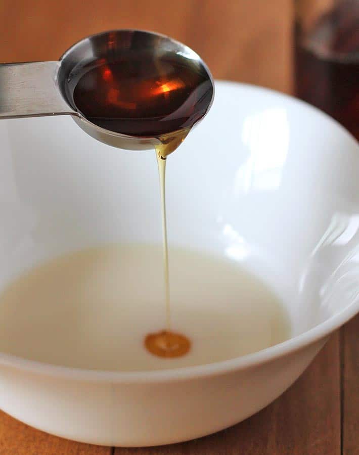 A tablespoon of maple syrup being poured into a white bowl to make a vegan egg wash.