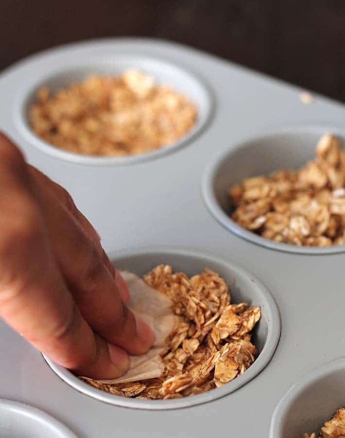 Oat mixture for fruit and yogurt granola cups being pressed into a muffin pan.