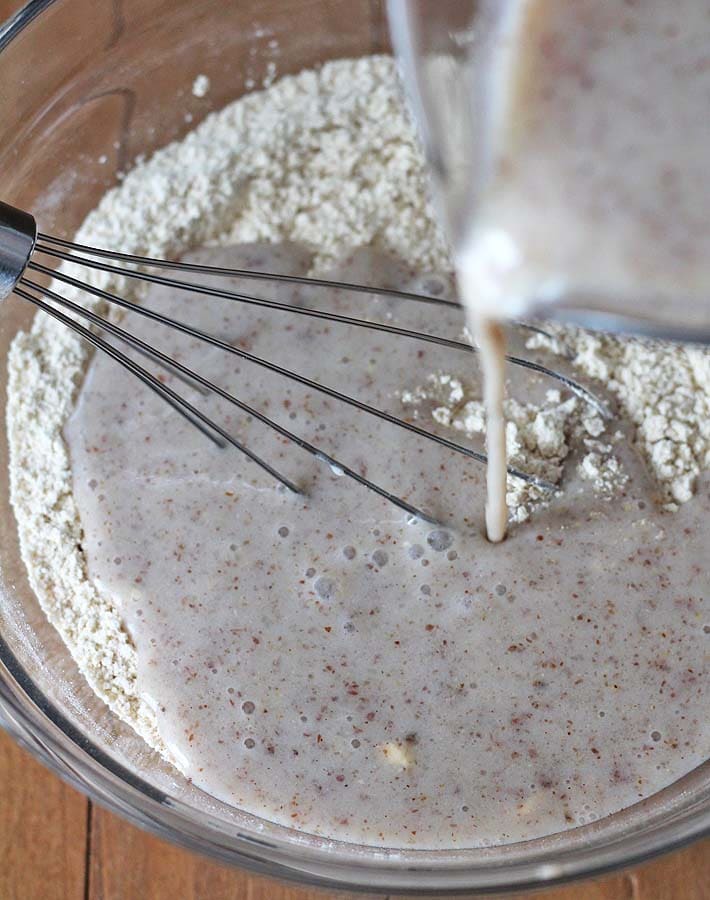The wet ingredients for Vegan Banana Pancakes being poured into a glass bowl that holds the dry ingredients for the recipe.