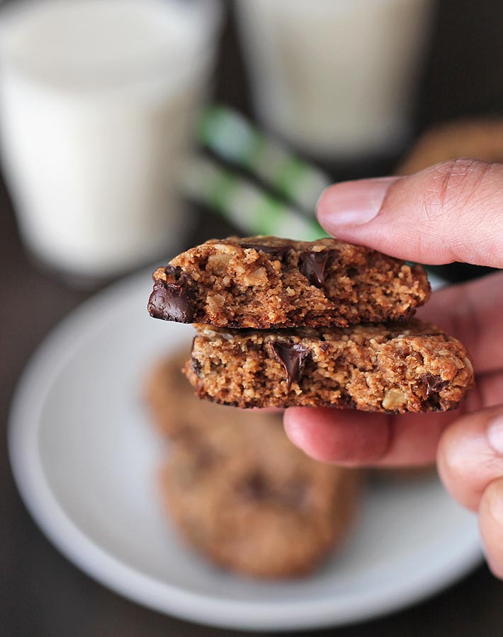 A hand holding a Peanut Butter Oatmeal Chocolate Chip Cookies that has been broken in half to show the inside texture.