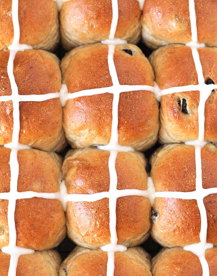 Overhead shot of fresh Vegan Hot Cross Buns that have just had icing crosses added to them.