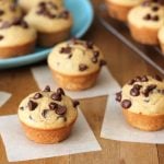 Four Mini Chocolate Chip Muffins sitting on individual parchment paper squares on a brown wooden table.