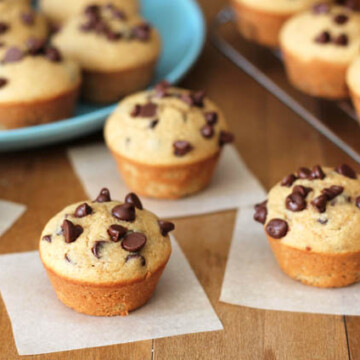 Four Mini Chocolate Chip Muffins sitting on individual parchment paper squares on a brown wooden table.