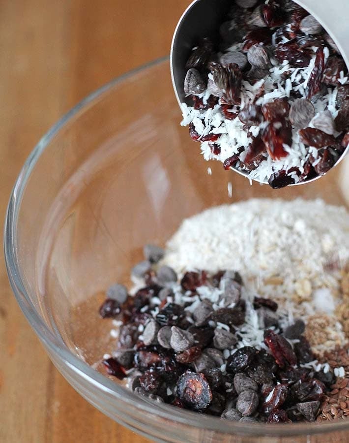 Add-in ingredients for vegan granola bars being poured into a glass bowl with the rest of the bar ingredients.