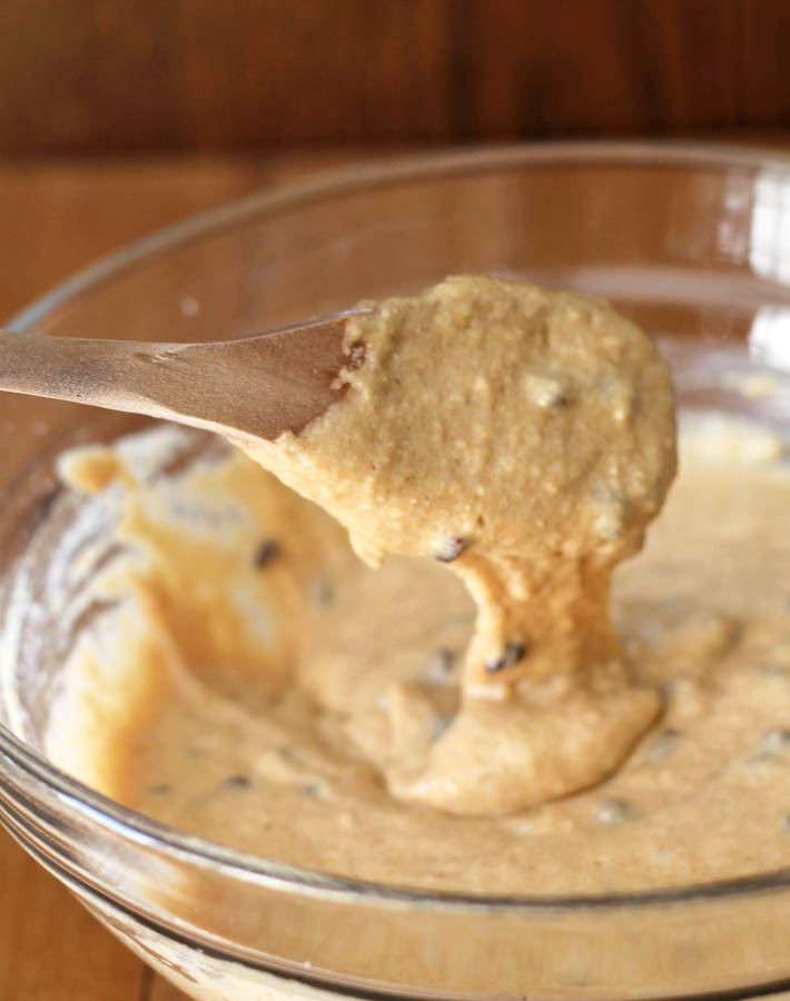 Batter for Mini Chocolate Chip Muffins in a glass bowl, batter is dripping off a wooden spoon that was used to stir the batter.
