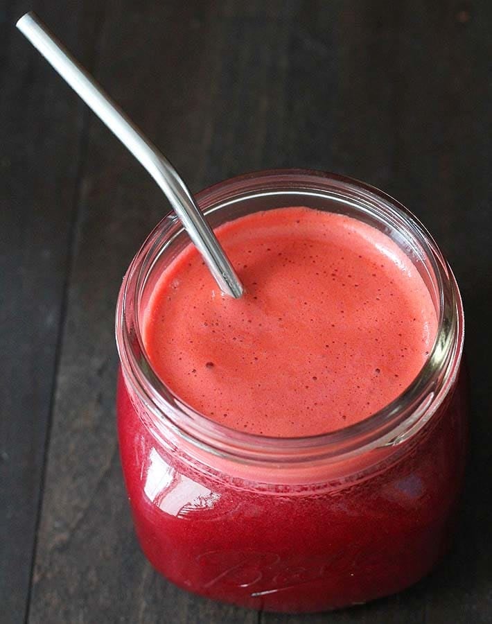 Overhead shot of Beet Carrot Apple Juice in a small glass with a stainless steel straw.