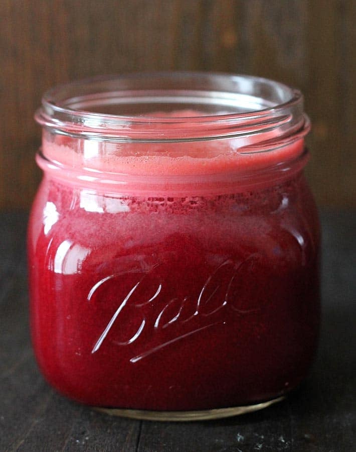 Beet Carrot Apple Juice in a Ball Mason jar sitting on a dark wood table.