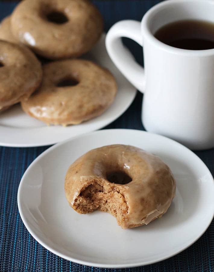 A maple doughnut on a white plate, the doughnut has a bite taken out of it.