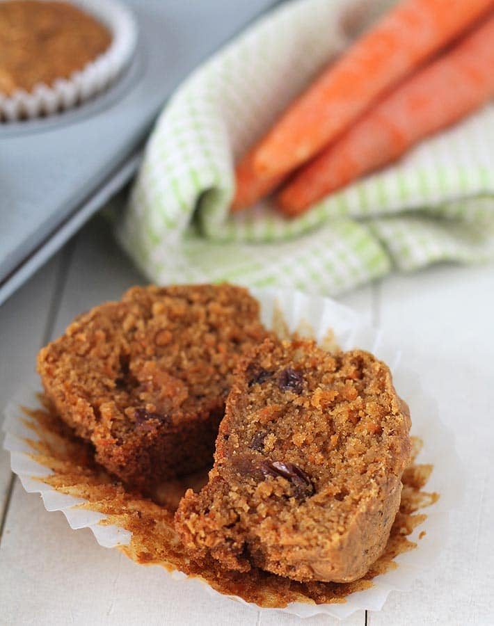 A carrot muffin on a table, it\'s split to show the soft inner texture of the muffin. 