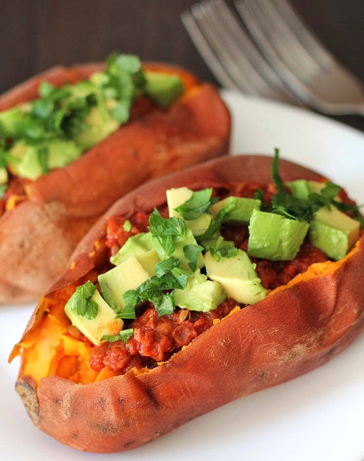 Mixture for lentil sloppy joes in a split sweet potato, mixture is topped with cubed avocado and chopped parsley.
