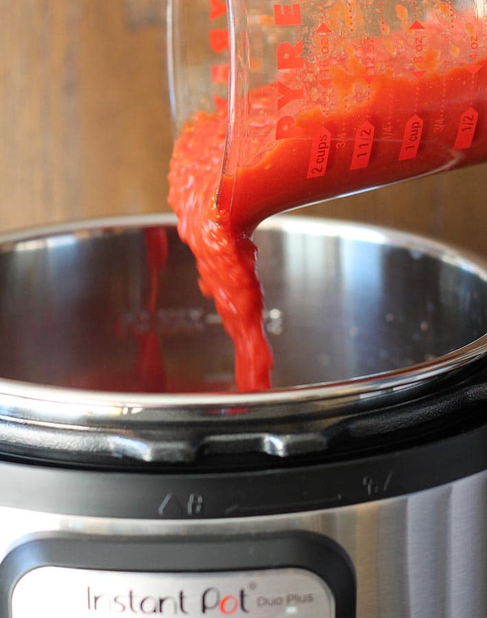 Crushed tomatoes being poured into an Instant Pot to make the filling for lentil sloppy joes sandwiches.