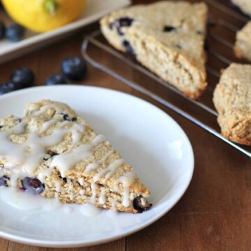 A lemon blueberry scone on a white plate, the plate is sitting on a brown wooden table.