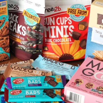 Several packages of packaged store-bought, allergy-friendly, nut-free snacks and treats sitting on a brown wood table.
