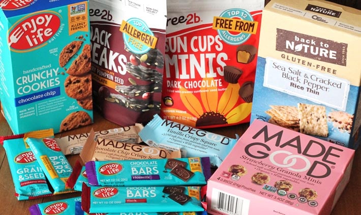 Several packages of packaged store-bought, allergy-friendly, nut-free snacks and treats sitting on a brown wood table.